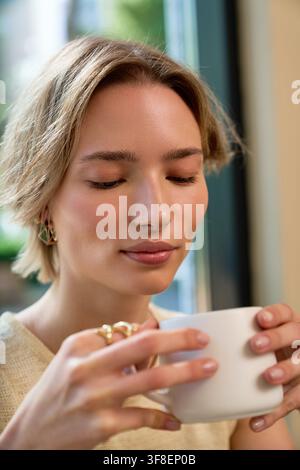 Donna elegante con capelli corti si rilassa e assapora la sua bevanda calda al bar Foto Stock