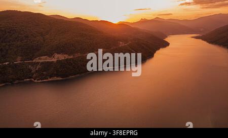 Vista aerea del bacino idrico di Zhinvali circondato da verdi colline montuose illuminate dalla calda luce dorata del tramonto in Georgia, una destinazione turistica scenografica Foto Stock