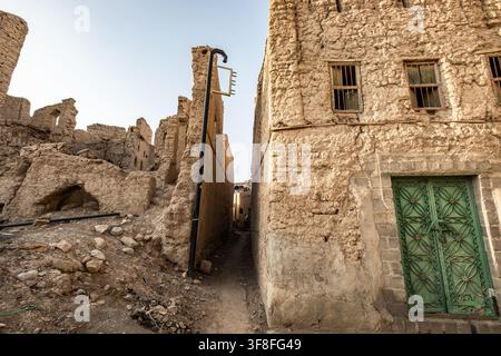 Antica casa in mattoni di fango con porta in legno verde tra le rovine a Nizwa, Oman Foto Stock