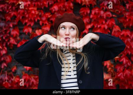 Ritratto femminile con fogliame rosso acceso, atmosfera allegra e vibrazioni autunnali. Foto Stock