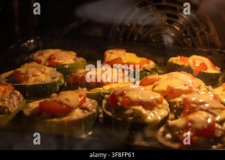 Fette di zucchine ripiene di carne che cuociono nel forno con formaggio fuso Foto Stock
