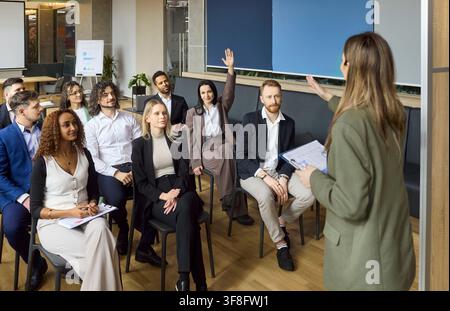 Relatrice femminile che guida un pubblico aziendale diversificato in un seminario interattivo in ufficio Foto Stock