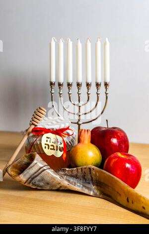Simboli di Rosh Hashanah che mostrano menorah, shofar, miele, mele e melograno su un tavolo di legno Foto Stock