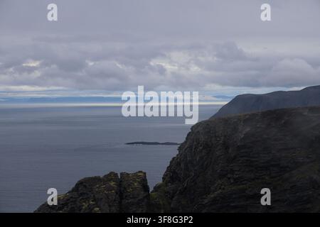 Maestose scogliere di roccia scura a Nordkapp che si affacciano sull'oceano vasto sotto cieli artici nuvolosi. Foto Stock