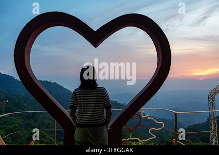 Forma a cuore che circonda una donna che osserva il tramonto nelle Kokol Hills Kota Kinabalu Sabah Borneo Malesia Foto Stock