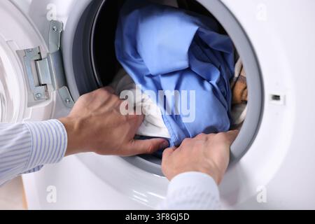 Uomo che mette i vestiti nella lavatrice, primo piano. Giorno della lavatrice Foto Stock