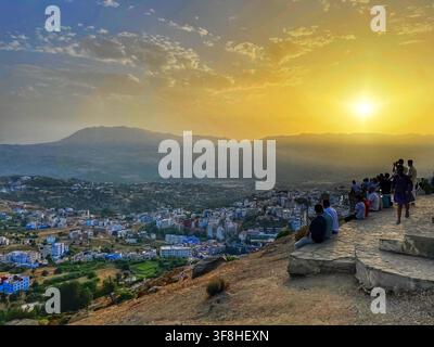 Visitatori che si rilassano su una collina che si affaccia sulla città blu di Chefchaouen, Marocco, mentre il sole tramonta sui Monti del Rif, catturato il 6 agosto 2025 Foto Stock