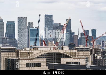 Vista della moderna skyline di Canary Wharf con numerosi grattacieli, facciate in vetro e gru edili sotto un cielo nuvoloso a Londra, Inghilterra, Unite Foto Stock