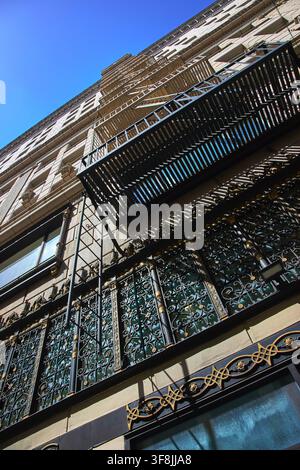 Facciata di edificio urbano ornato con scala antincendio e ferri decorativi alla luce del sole Foto Stock