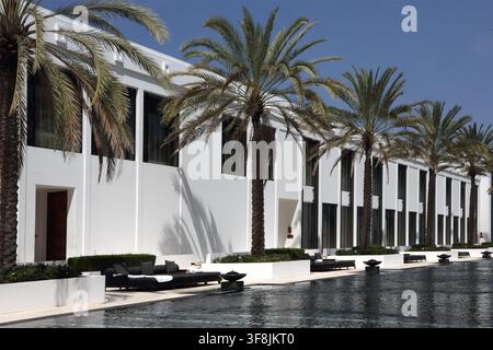 Piscina a sfioro fiancheggiata da palme da dattero con sdraio al The Chedi Hotel Muscat, Sultanato dell'Oman Foto Stock