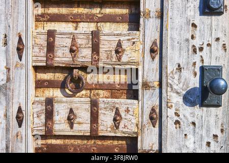 Primo piano di una porta di legno consumata con ferri e maniglia rustica ad anello Foto Stock