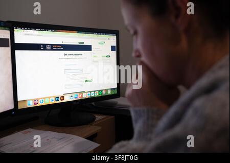 SYDNEY - 11 AGOSTO 2026: Una donna australiana matura preoccupata si siede nel suo ufficio di casa mentre adempie al suo dovere civico nazionale utilizzando un desktop per compilare Foto Stock