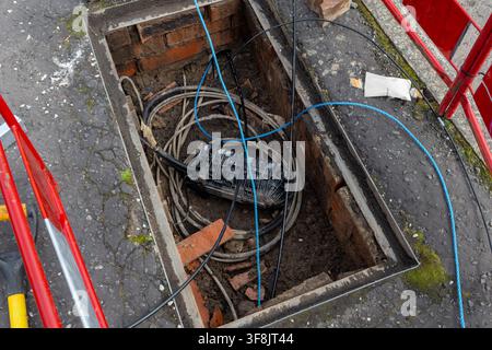 Chiusura in fibra ottica nera si trova tra cavi arrotolati e corde di traino blu all'interno di una camera di telecomunicazioni aperta rivestita in mattoni. Barriere rosse e bianche incorniciano Foto Stock