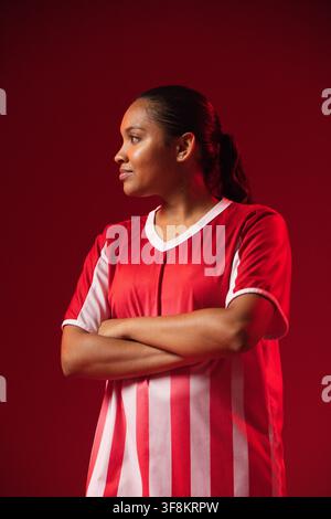 Donna africana in piedi di fronte a sinistra in studio che indossa una maglia sportiva rosso-bianca, un orecchino borchiato e un elastico per capelli Foto Stock