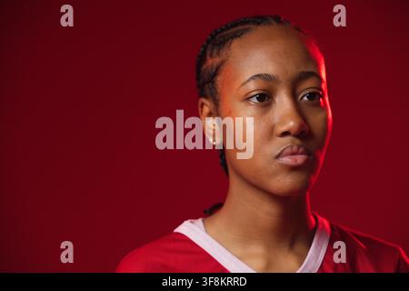 Donna sui 20 anni con maglietta sportiva rossa con colletto bianco, trecce e orecchini a cerchio, in posa in studio, spazio per il testo Foto Stock