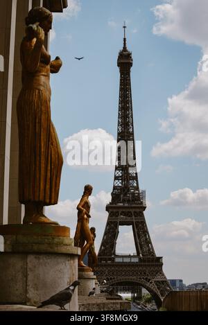 Parigi, Francia - 06 maggio 2022: Vista della Torre Eiffel incorniciata da statue dorate e pilastri di pietra sotto un cielo azzurro con nuvole sparse, con un piccione Foto Stock