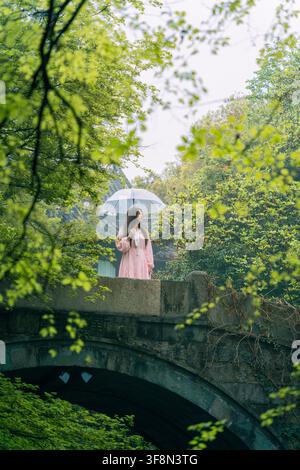 Donna con cappello che tiene un ombrello su un antico ponte di pietra, vista posteriore, Liulang Wenying, Hangzhou Foto Stock