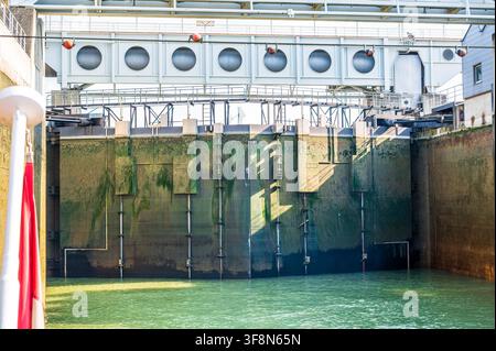 Foto verticale di una grande porta di chiuse sul Danubio a Vienna, Austria. Le massicce pareti in metallo e cemento della camera di chiuse sono macchiate di alghe Foto Stock