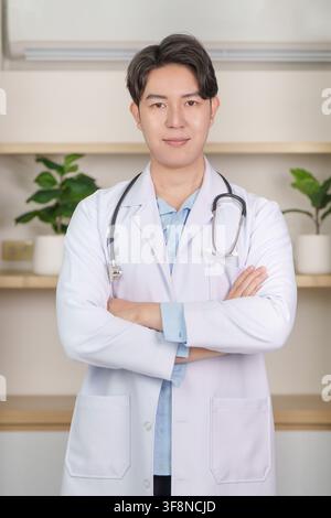 Medico asiatico con camice bianco e stetoscopio, braccia incrociate in clinica Foto Stock