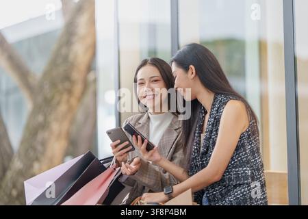 Donne asiatiche che controllano gli smartphone con borse della spesa all'aperto per i saldi del Black Friday Foto Stock