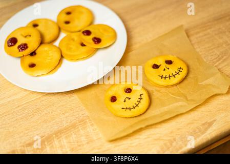 Biscotti fatti in casa di colore marrone dorato a forma di divertenti volti di zucca su carta da forno prima della decorazione Foto Stock
