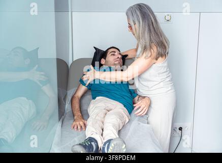 Fisioterapista che controlla i progressi della riabilitazione di un giovane disabile sdraiato sul lettino di esame Foto Stock