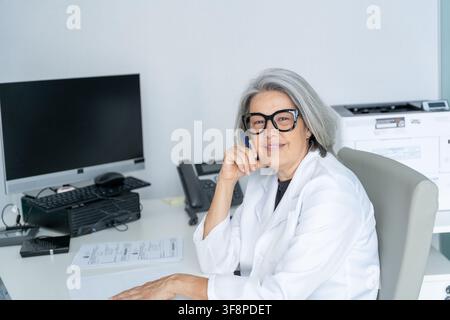 Medica esperta con occhiali e camice bianca, che lavora nel suo studio medico Foto Stock