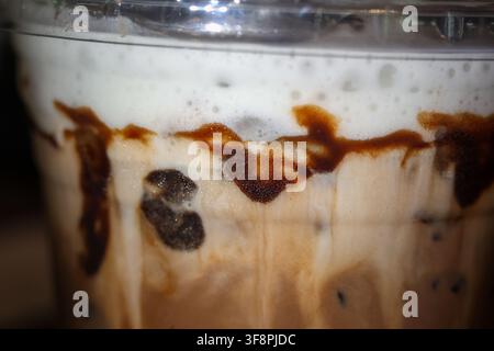 Una bevanda caffè ghiacciata con schiuma cremosa e vortice di cioccolato ricoperta di schiuma, primo piano della trama che mostra il ghiaccio che si scioglie e la ricca bevanda, indulgente col Foto Stock