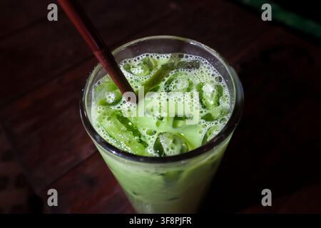 Un latte matcha ghiacciato con schiuma vellutata e cubetti di ghiaccio in un bicchiere alto, bevanda rinfrescante al tè verde con cannuccia, atmosfera accogliente e texture in primo piano Foto Stock