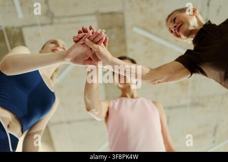 Donne caucasiche diverse che impilano le mani in palestra, mostrando unità e sostegno. L'immagine rappresenta l'empowerment femminile e la comunità fitness, adatta al marketing del benessere, vista dall'alto Foto Stock
