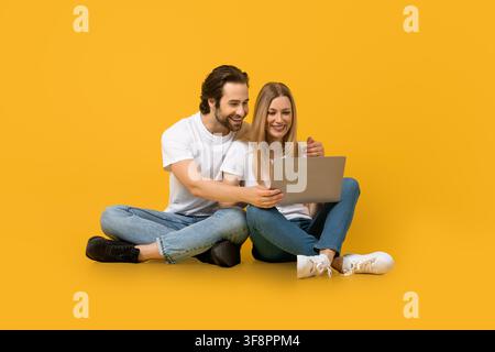 Giovane coppia felice che sorride e lavora insieme su un laptop, ambiente interno, concetto aziendale Foto Stock