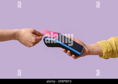 Mano del cliente che inserisce una carta di credito rosa in un terminale di pagamento blu per una transazione su uno sfondo viola Foto Stock