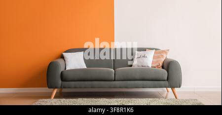 Divano moderno grigio con cuscini decorativi contro un muro bicolore arancione e bianco in un interno di soggiorno contemporaneo Foto Stock