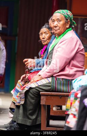 Namche, Nepal – 16 agosto 2022: Vista di anziane donne Sherpa sedute su una panchina di legno, indossanti abiti tradizionali e tenendo rosari durante un Foto Stock