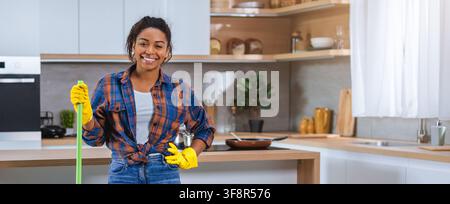 Donna nera sorridente che pulisce la cucina con mocio e guanti, concetto di pulizia domestica Foto Stock