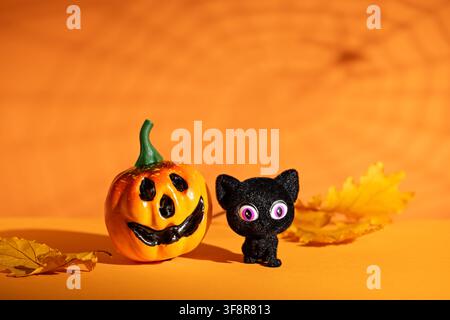Jack o lantern e gatto nero con foglie d'autunno su sfondo arancione per un grazioso biglietto o poster per feste di Halloween Foto Stock