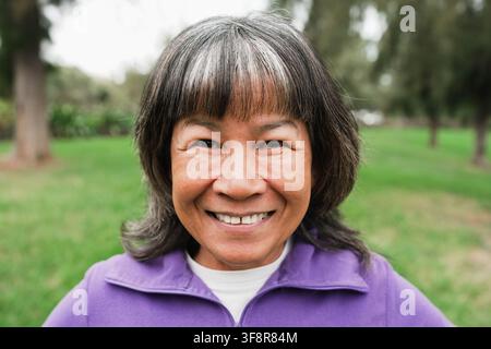 Felice donna asiatica anziana che sorride alla telecamera dopo l'allenamento di yoga all'aperto - Concetto di sport e stile di vita sano Foto Stock