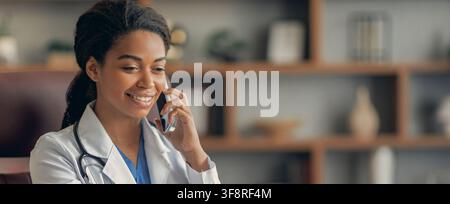 Dottore nera sorridente che parla al telefono, concetto di assistenza sanitaria Foto Stock