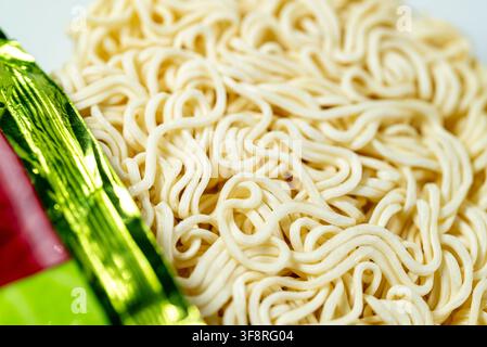 Preparazione di cibo veloce asiatico che mostra pasta Ramen secca appoggiata accanto alla sua confezione lucida Foto Stock