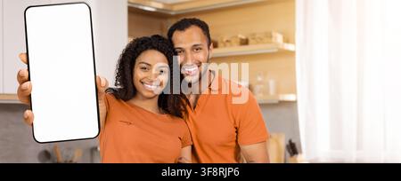 Coppia afroamericana felice che sorride e tiene uno smartphone in cucina, concetto familiare Foto Stock