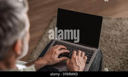 Uomo anziano irriconoscibile che digita su un laptop a casa, concentrato sul lavoro Foto Stock