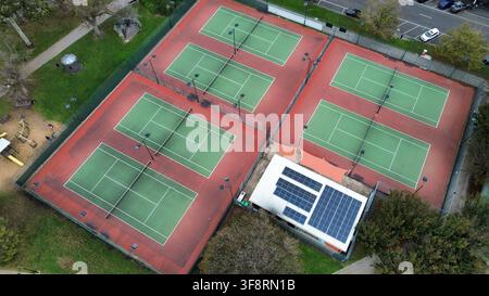 Più campi da tennis con reti e luci per attività sportive, che mostrano un edificio con pannelli solari sul tetto Foto Stock