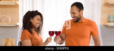 Coppia afroamericana felice che brinda con bicchieri di vino a casa, serata romantica Foto Stock