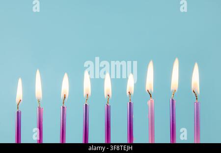 9 candele di compleanno color rosa metallico e viola che bruciano in fila isolate su sfondo blu. Concetto di design per biglietti di auguri di compleanno. Foto Stock