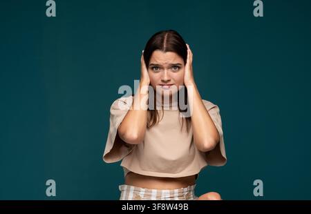 Giovane donna che si copre le orecchie, si sente infastidita e stressata dal rumore forte, lotta con frustrazione e disagio Foto Stock