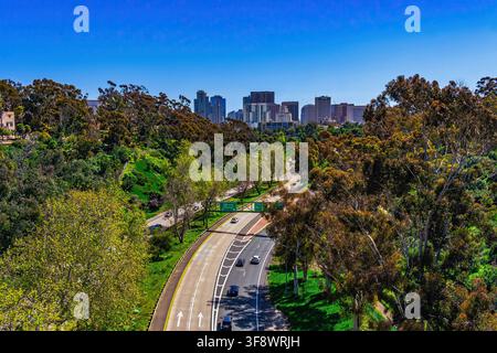 Vista elevata di un'autostrada curva attraverso un parco con lo skyline del centro in lontananza. Balboa Park, San Diego, California, Stati Uniti Foto Stock