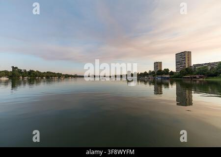 Una vista grandangolare del calmo fiume Sava a Belgrado, in Serbia, durante un tranquillo tramonto. Edifici residenziali alti e alberi verdi lungo il fiume Foto Stock