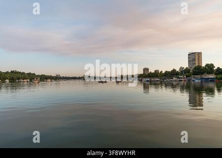 Una vista tranquilla del tramonto sul fiume Sava a Belgrado, in Serbia, con piccole barche ormeggiate lungo le rive e riflessi sull'acqua specchiata. Un ta Foto Stock