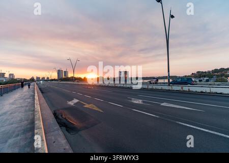 Una vista grandangolare di un ponte cittadino a Belgrado, in Serbia, durante un tramonto vivace. La strada è segnalata con frecce che puntano verso l'orizzonte luminoso, wh Foto Stock