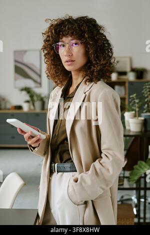 Ritratto di una donna biracial che tiene uno smartphone in un ufficio moderno Foto Stock